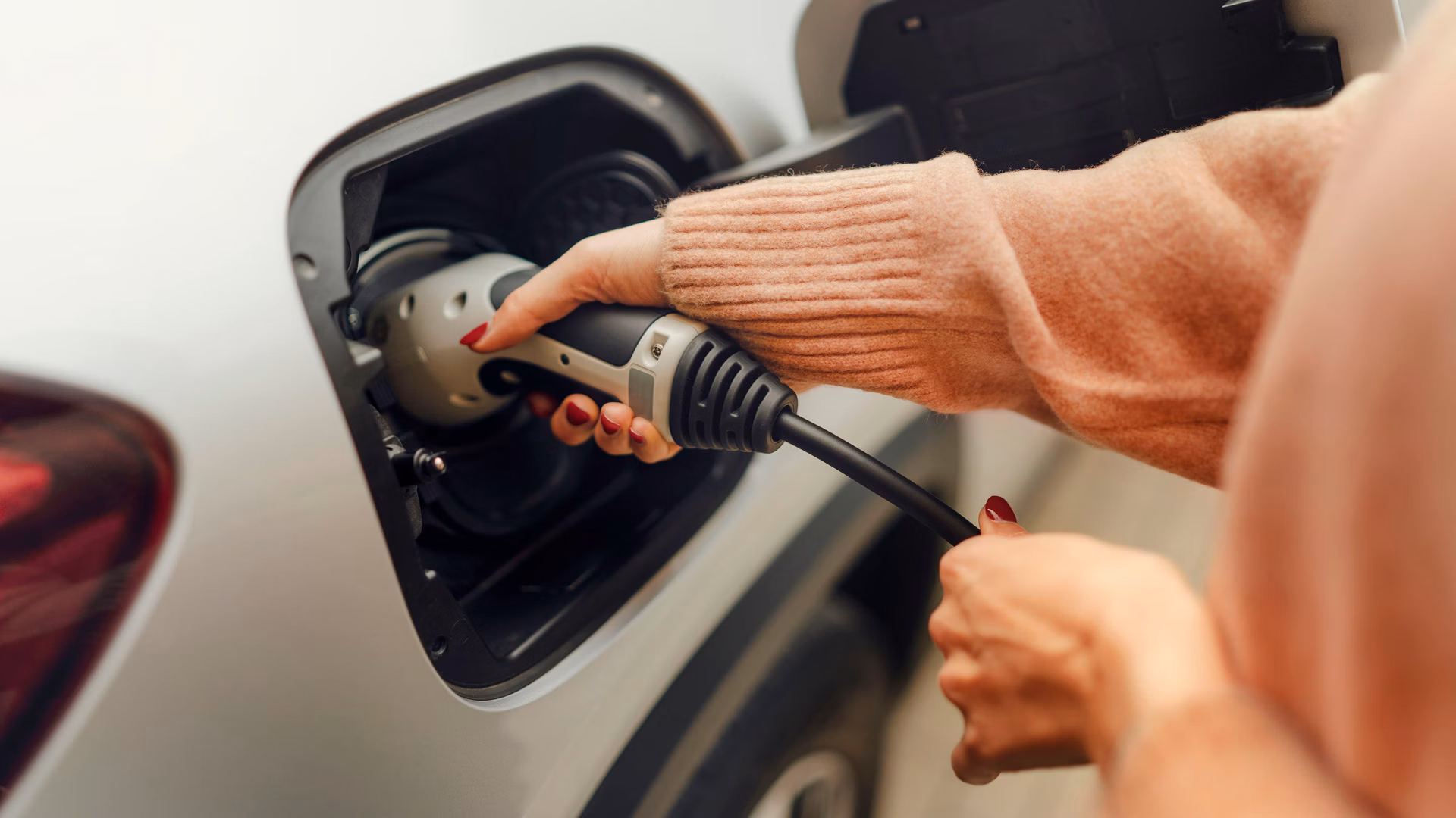Person steckt ein Ladekabel in den Anschluss eines Elektroautos.