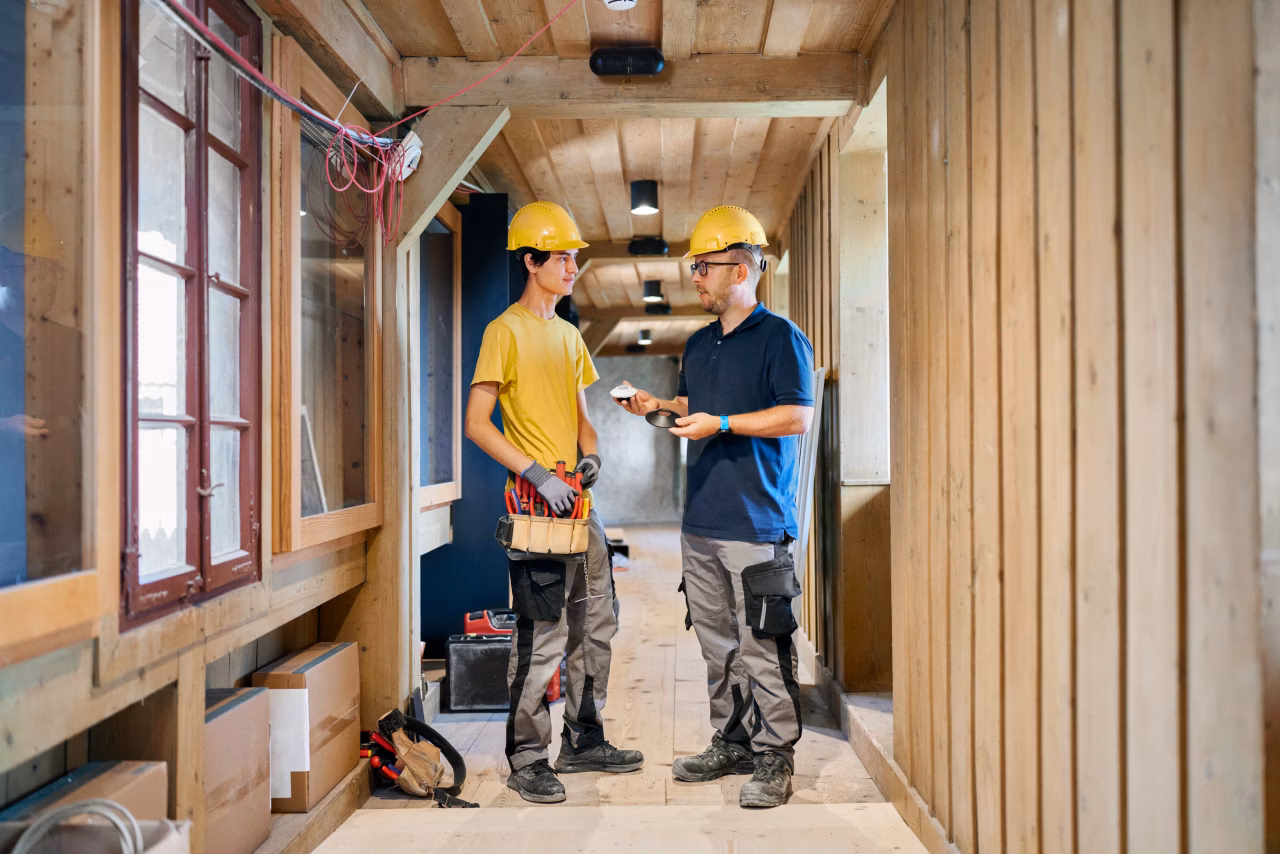 Zwei Handwerker der Elektro Winter AG mit Schutzhelmen besprechen Arbeiten in einem Innenraum aus Holz.