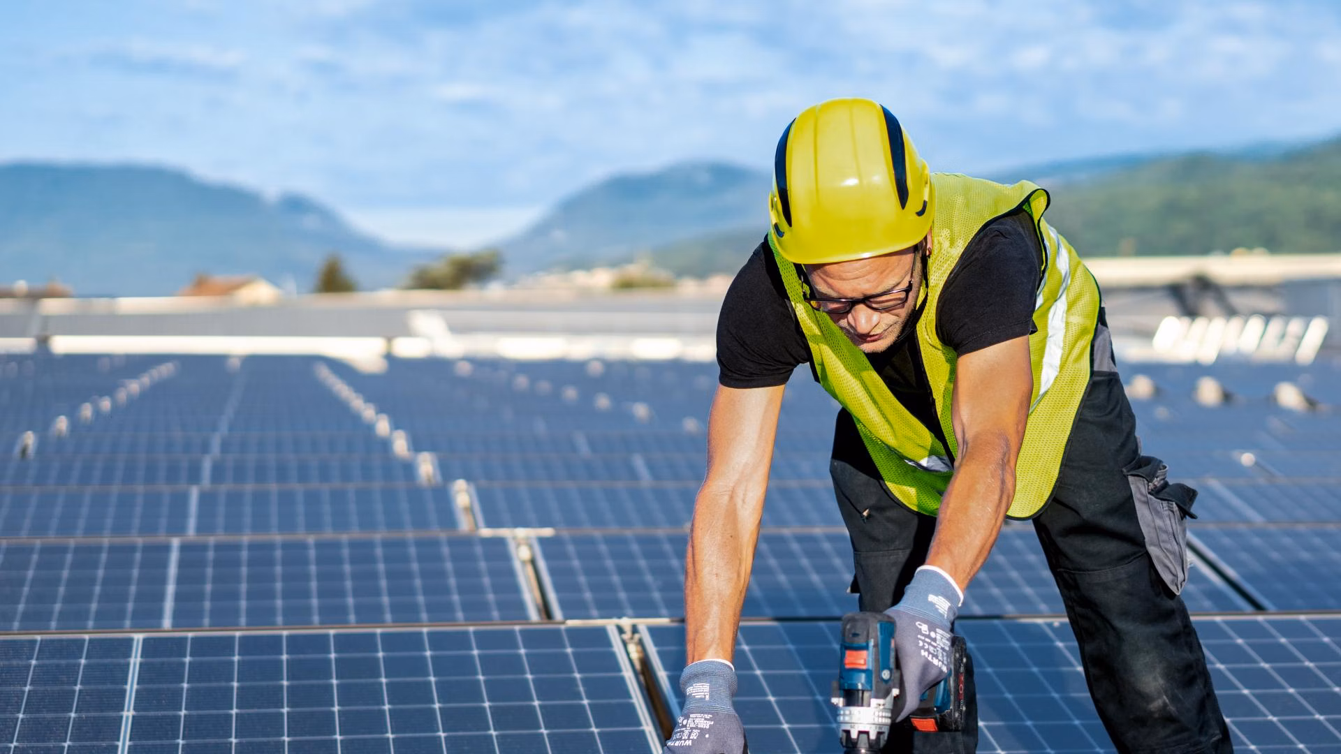 Arbeiter mit Schutzhelm und Warnweste montiert Solarmodule auf einem Dach.