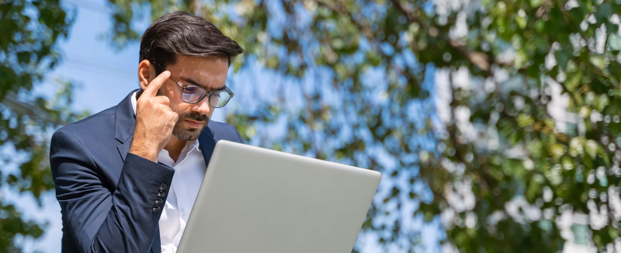 Mann im Anzug arbeitet im Freien mit Laptop und Smartphone.