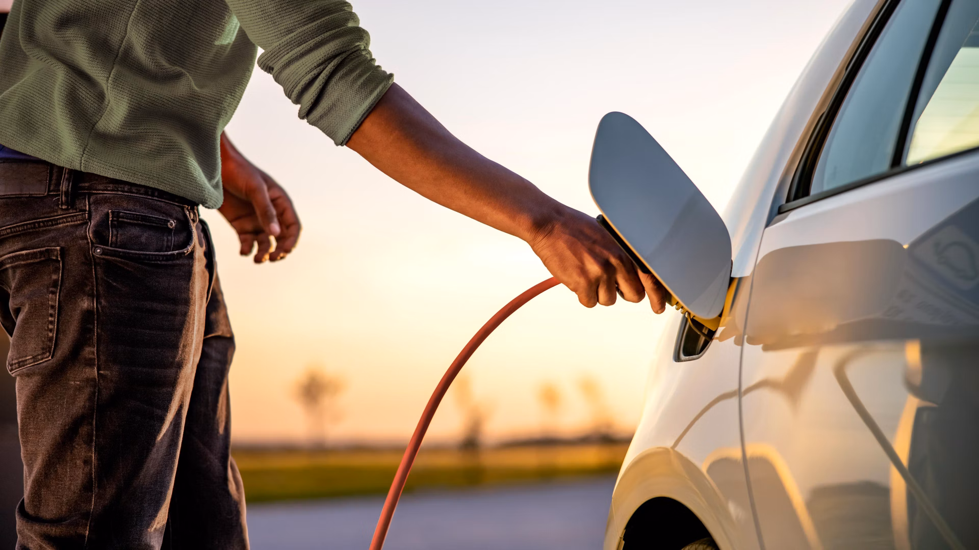 Person steckt ein Ladekabel in ein weisses Elektroauto.