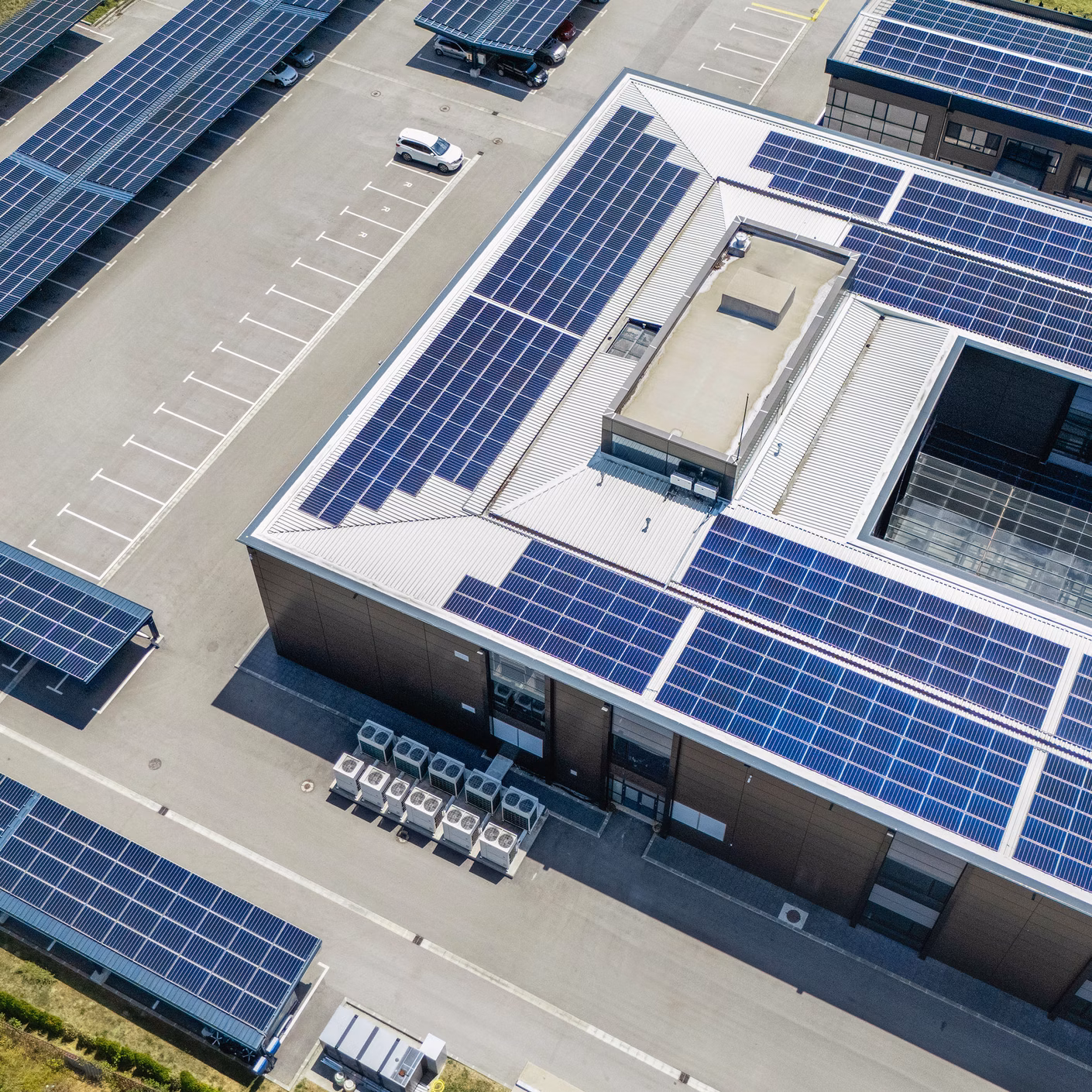 Vista con drone di un edificio industriale con diversi impianti fotovoltaici sui tetti e sopra i parcheggi