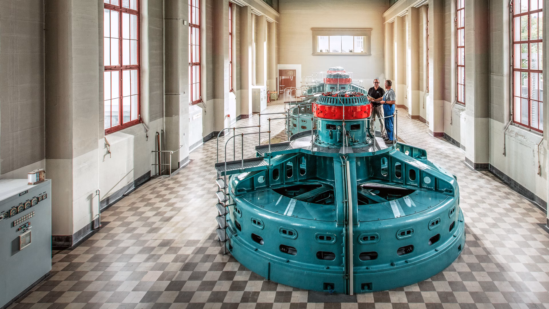 Sala turbine con macchina color turchese e alte finestre in un edificio industriale storico