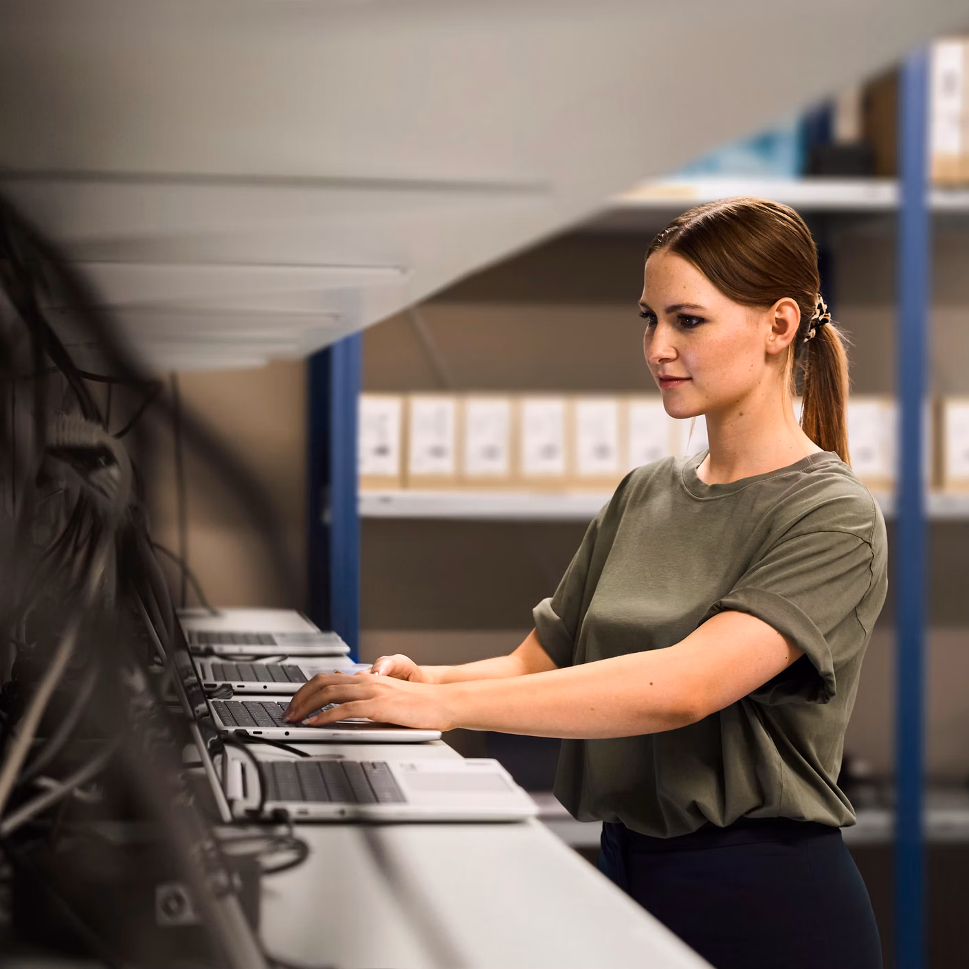 Woman operating several monitors in a technical room with shelves in the background