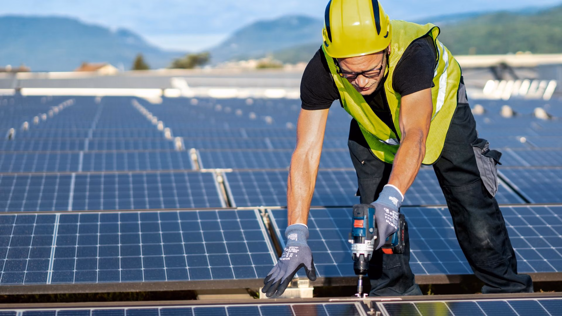 Arbeiter mit Schutzhelm und Warnweste montiert Solarmodule auf einem Dach.