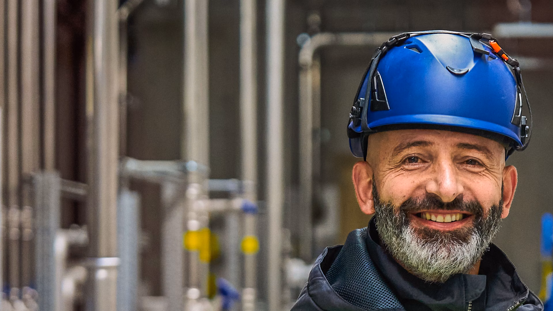 Mitarbeiter mit Helm und Warnweste in einem Technikraum mit Rohrleitungen und Ventilen