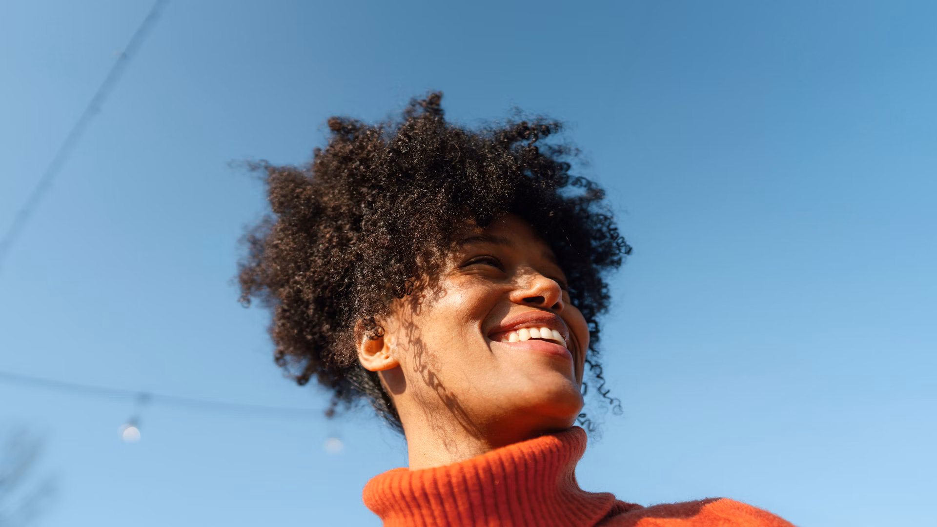 Lächelnde Person in rotem Rollkragenpullover vor blauem Himmel