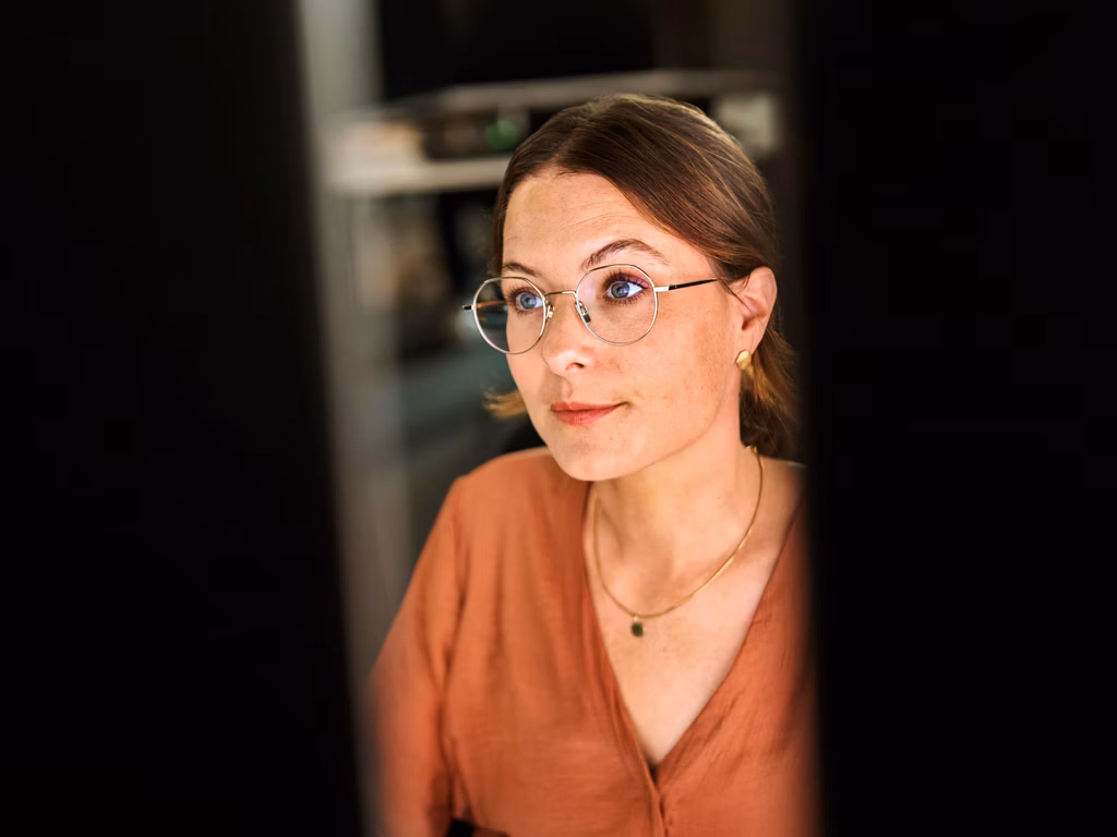 Frau mit Brille arbeitet konzentriert an mehreren Bildschirmen.