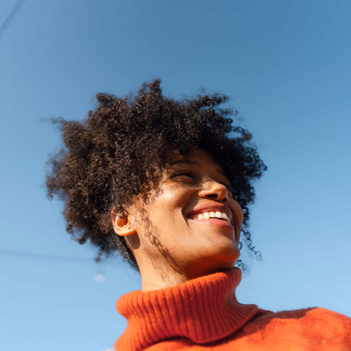 Lächelnde Person in rotem Rollkragenpullover vor blauem Himmel