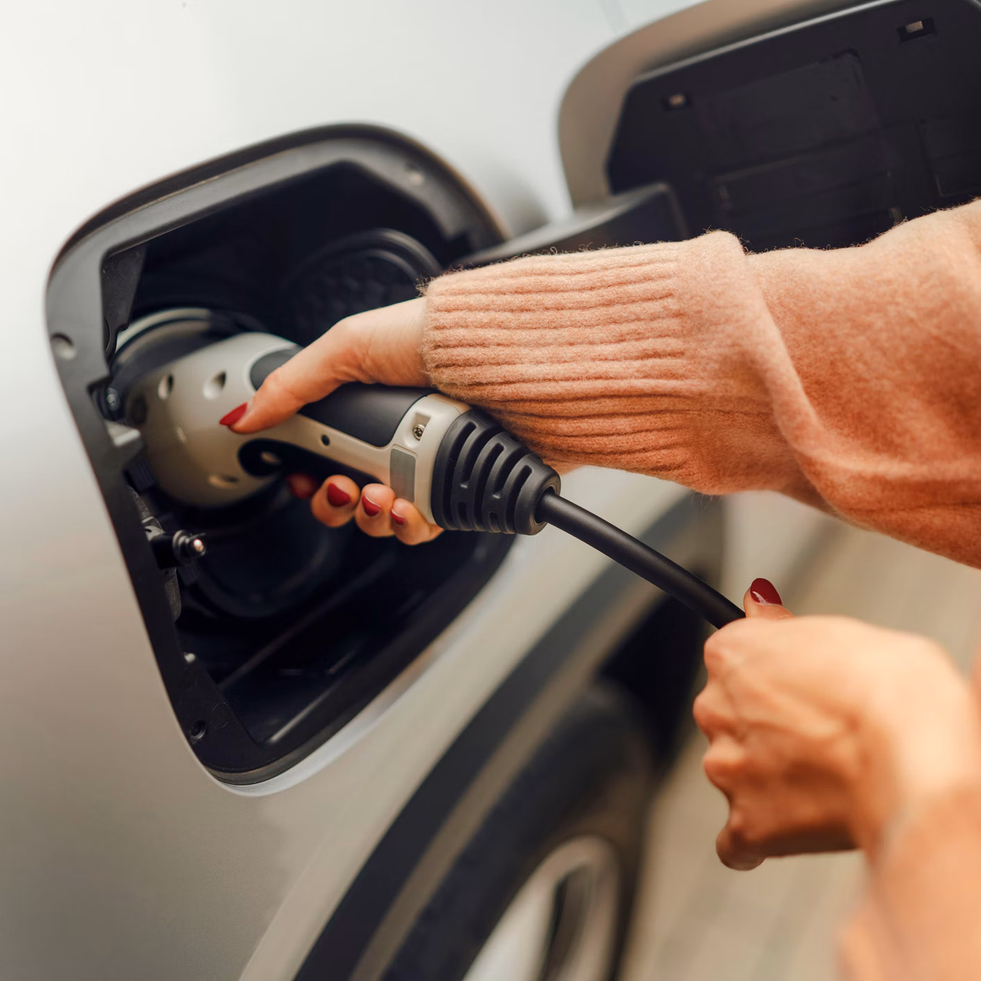 Una persona inserisce un cavo di ricarica nella presa di un’auto elettrica.
