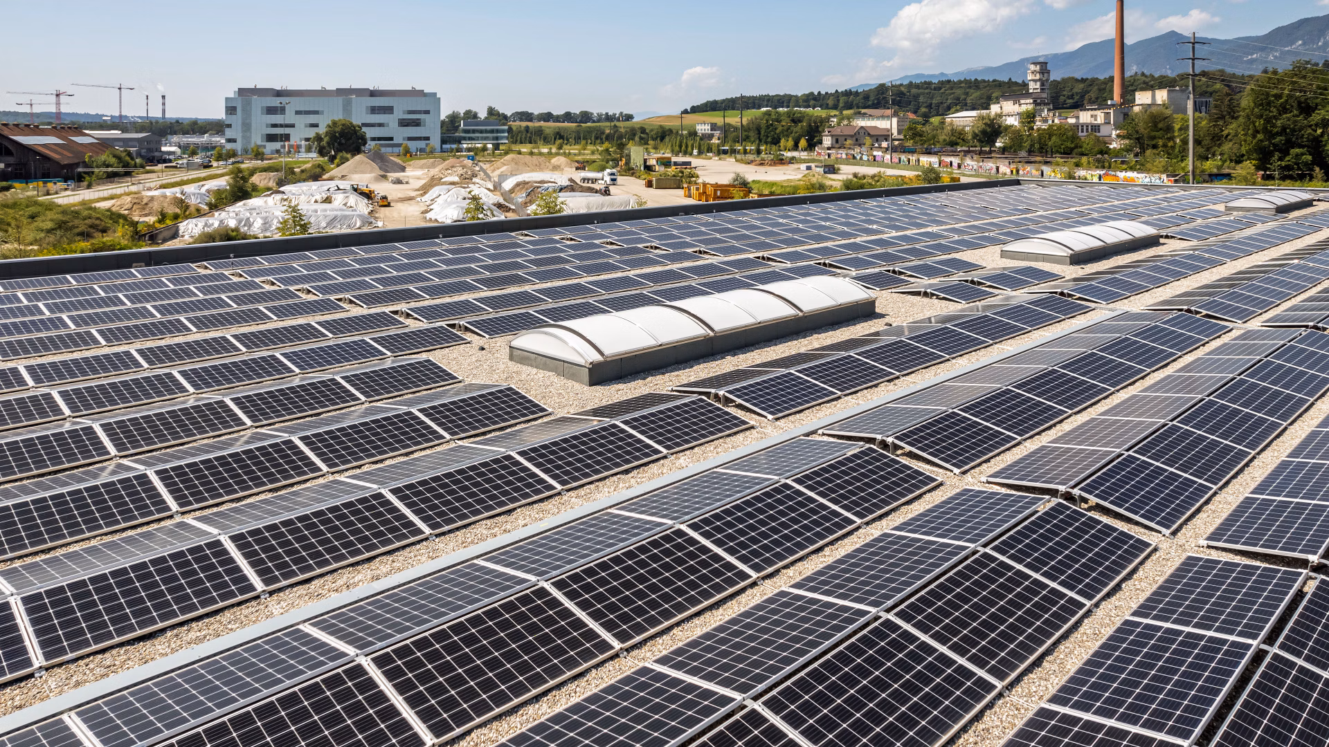 Photovoltaic system on a large flat roof with industrial buildings in the background