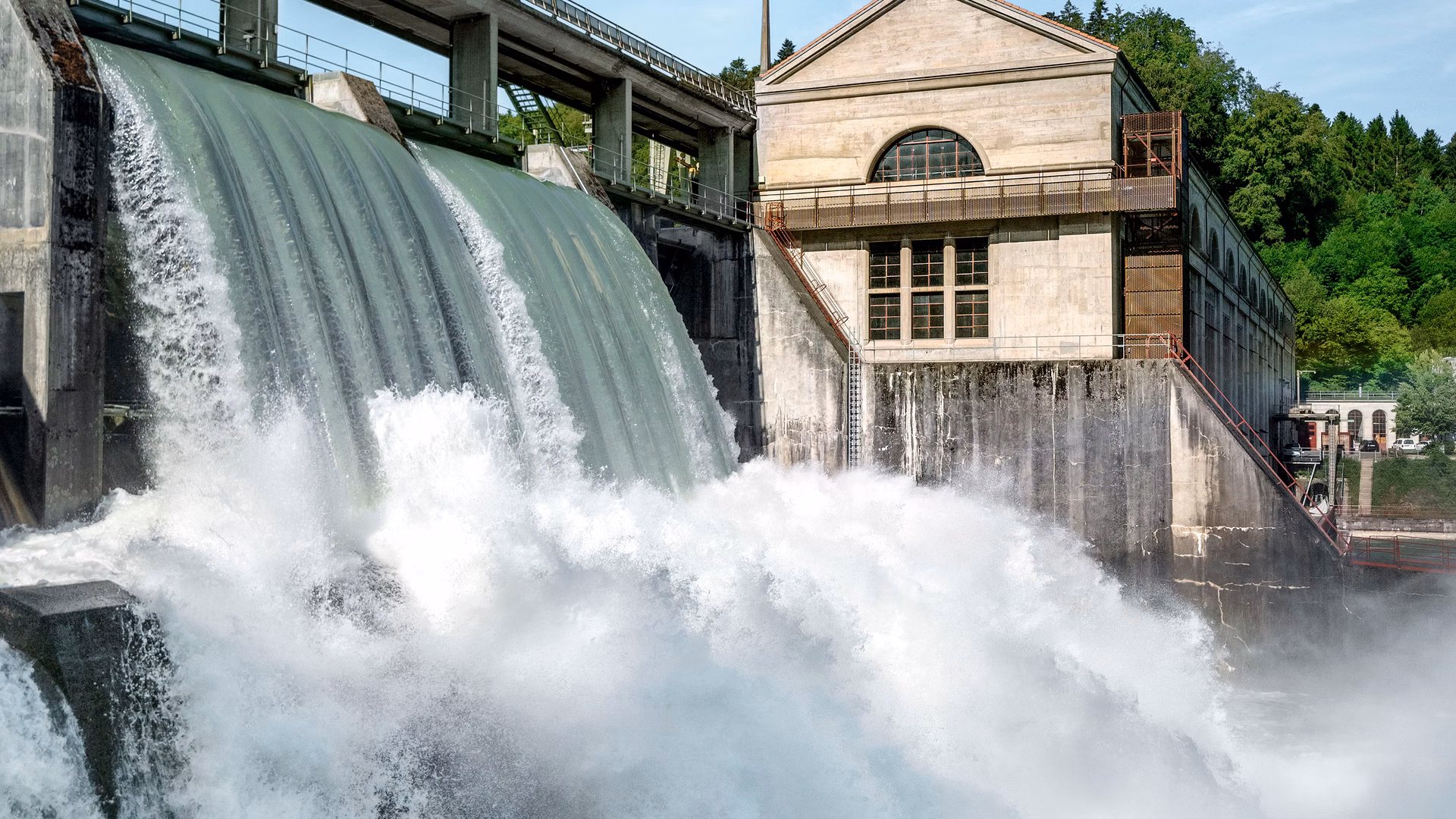 Wasserkraftwerk mit starkem Wasserabfluss über ein Wehr neben einem Betriebsgebäude.